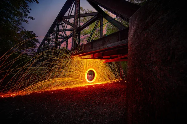 Espiral de faíscas de lã de aço laranja sob grande ponte metálica — Fotografia de Stock