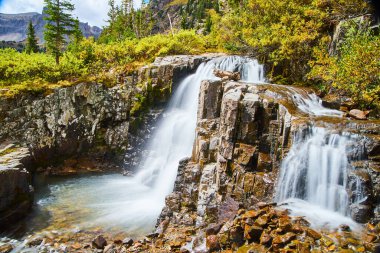 Şelalenin yakın plan görüntüsü, renkli kayalarla kaplı bir kova suya dönüşüyor.