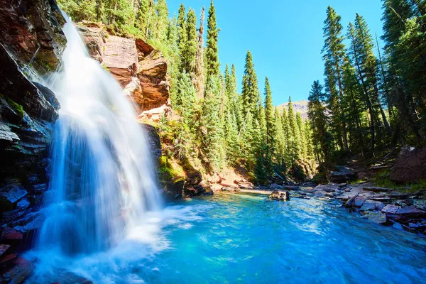 Вид збоку мальовничого блакитного водоспаду, встромленого в ущелину в горах, оточених сосновими деревами — стокове фото