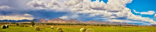 Panorama di balle di fieno in campo con grande catena montuosa e nuvole di tempesta che piovono — Foto Stock