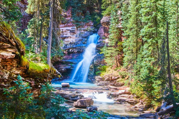 Vista incrível da cachoeira escondida no fundo do desfiladeiro com rochas vermelhas, lençóis de musgo e pinheiros — Fotografia de Stock