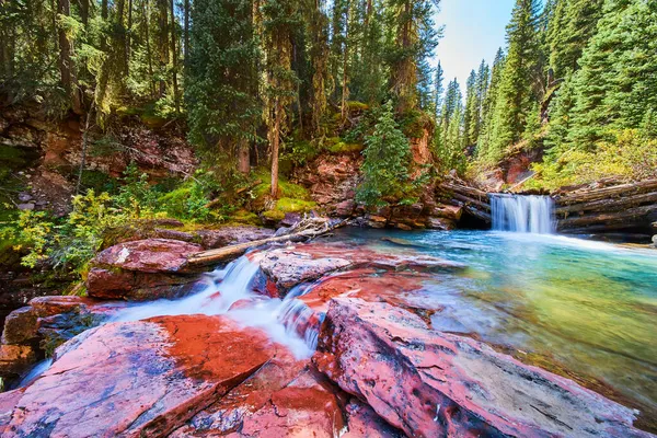 Majestuosas cascadas sobre rocas rojas en cañón de musgosas rocas y pinos —  Fotos de Stock