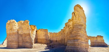 Çölden sarkan beyaz ve bej renkli dikey kayalar ve parlak mavi gökyüzü manzarası.