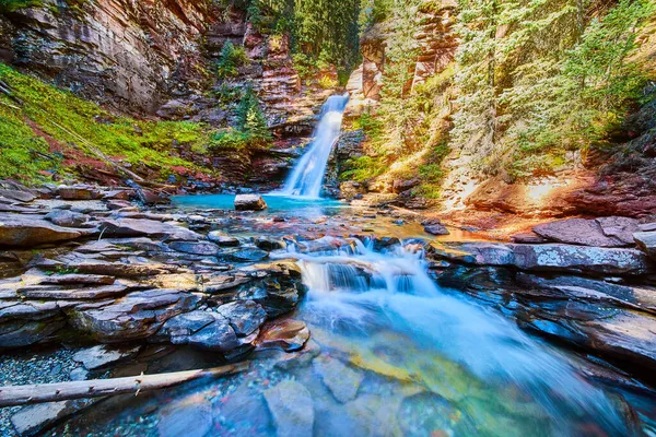 Waterfall tucked into canyon with vibrant blue water and river rocks — Stock Photo, Image