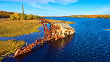 Altın saatinde gölde batık bir çalı mavi bir gökyüzü ve arka planda düşen ağaçlarla dolu bir silo.