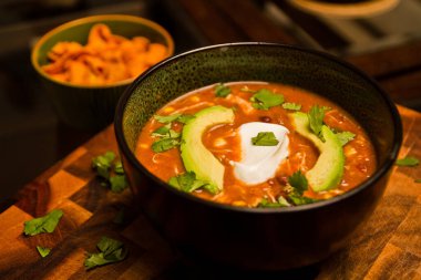 Kişniş ekşi kremalı nefis tavuk enchilada çorbası ve ahşap kesim tahtasındaki siyah kasede avokado.