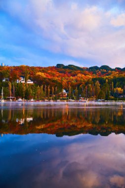 Sonbahar ağaçları, kırmızı turuncu ve yeşil nehirlerin diğer yakasında mavi gökyüzü ve güneş doğarken mor bulutlar ile birlikte suya yansıyor.