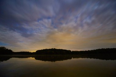 Mavi ve sarı gökyüzü şafak vakti Gölün ötesinde bir orman ve bir göl