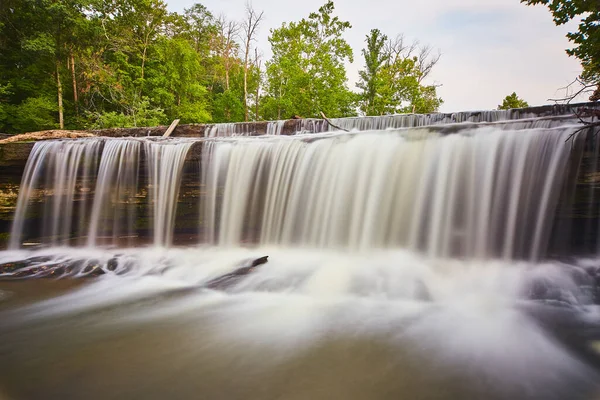 Smidigt vattenfall med bassäng nedanför och grön skog och himmel ovanför — Stockfoto
