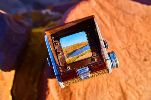 Felsen mit einer Kamera darauf und einem Sucher, der einen von umstürzenden Bäumen umgebenen See zeigt — Stockfoto