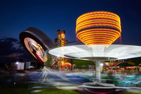 Balades en vrille et lumières brillantes lors d'un carnaval ou d'une foire au crépuscule — Photo