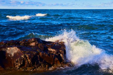 Uzakta çarpan bir dalganın ve yeşil bir yelkenlinin spreyiyle klasik rock.