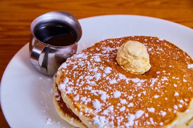 Klasik krep yığını üzerine pudra şekeri serpiştirilmiş ve üzerine tereyağı ve şurup serpilmiş.