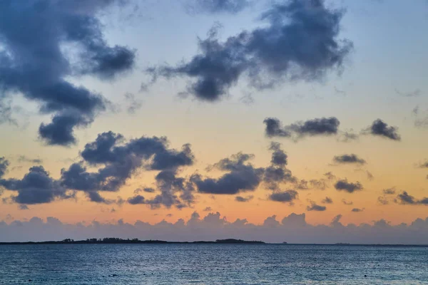 Pôr do sol no oceano com pequena ilha e pequenas nuvens escuras — Fotografia de Stock