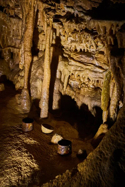 Gamla rostade dryckeskoppar på grottgrunden omgivna av stalagmiter och stalaktiter — Stockfoto
