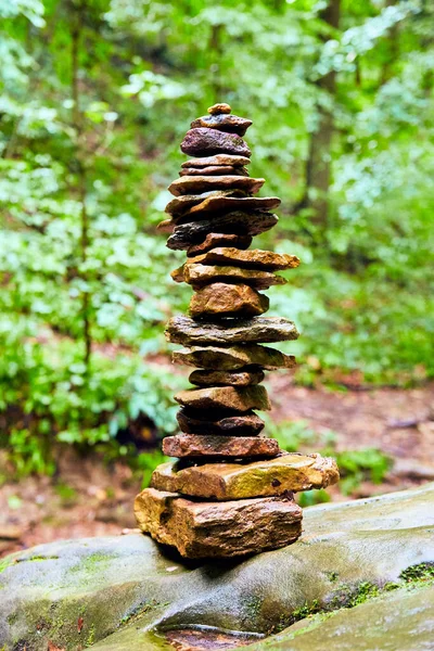 Cairn stack of small stones against bright green woods — Stock Photo, Image
