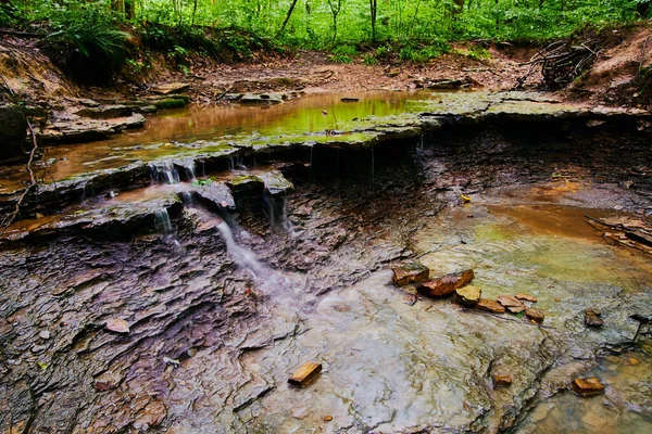 Мелкое русло реки с коричневыми камнями и небольшим водопадом — стоковое фото