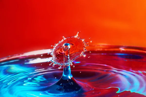 Két vízcsepp ütközik a kék víz piros háttér — Stock Fotó