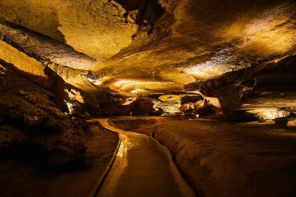 Walking path through large tourist cave with orange lights — Stock Photo, Image