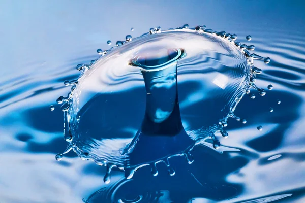 Large splash and ripples as two water drops hit in the air on blue water — Stock Photo, Image