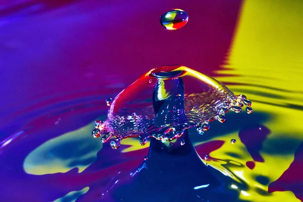 Gota de água prestes a atingir um cogumelo de água na superfície roxa e amarela — Fotografia de Stock