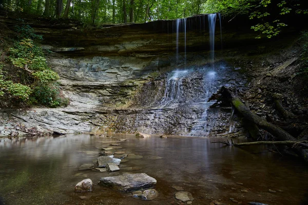 Cascada que cae en cascada sobre roca desnuda y luego en una cuenca dentro de un bosque —  Fotos de Stock