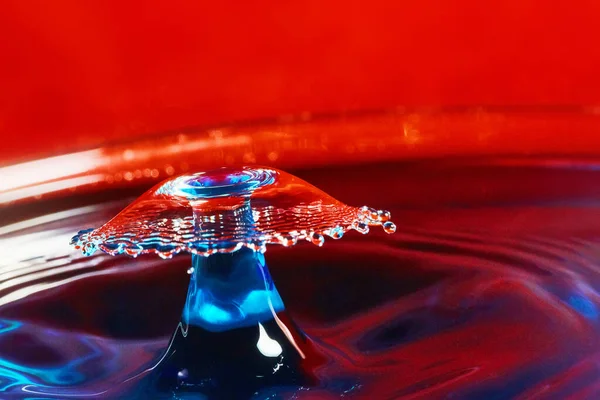 Acqua blu con due gocce d'acqua che colpiscono in aria sullo sfondo rosso — Foto Stock