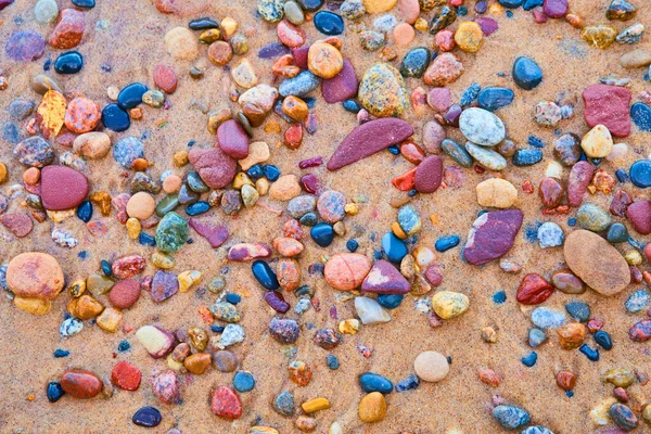 Parlak kırmızı, siyah, mavi, pembe ve mor renkli taşlar kumlu bir kıyıya karşı — Stok fotoğraf