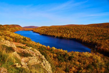 Bulutların arasında göl var. Sonu gelmeyen ormanlarla çevrili. Sol altta kaya var.