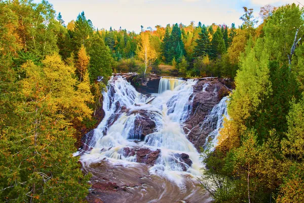 树栖息在瀑布的中央，瀑布被突出的岩石和秋天色的森林及其石盆打破了 — 图库照片