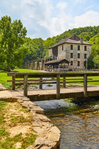 Старая каменная мельница с деревянным пешеходным мостом через крошечный ручей — стоковое фото