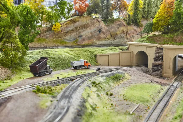 Miniature trucks with a train track, gravel road, and concrete overpass — Stock Photo, Image
