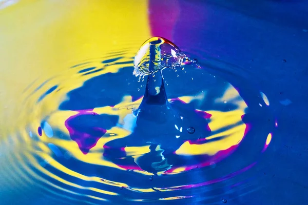 Água azul, roxa e amarela com ondulações e duas gotas de água batendo juntas — Fotografia de Stock