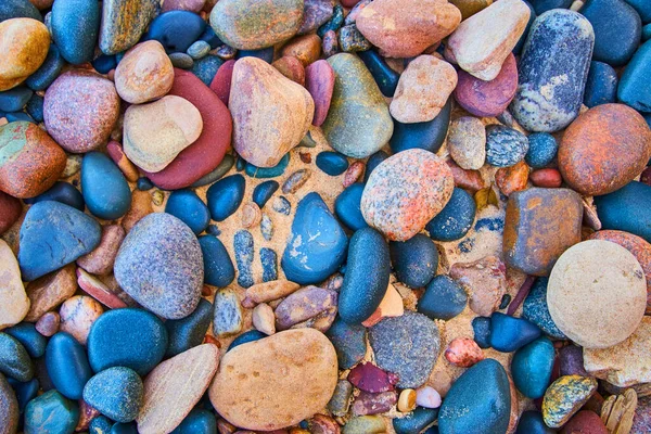 Smooth multicolored stones against a sandy beach — Stock Photo, Image