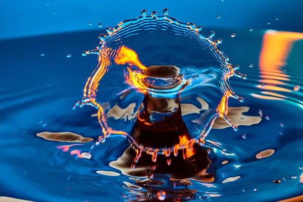 Splash av blått med en lysande orange vattendroppe — Stockfoto