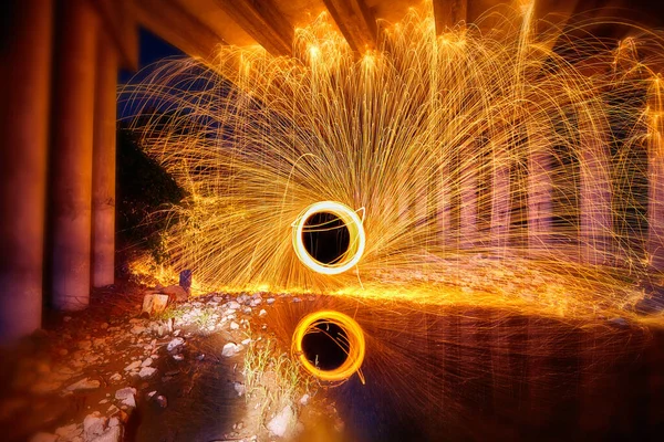 Portal żółto-białych iskier światła z wełny stalowej odbitych w wodzie pod betonowym mostem — Zdjęcie stockowe