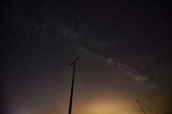 Město září hvězdnou noční oblohou a siluetou telefonních sloupů — Stock fotografie