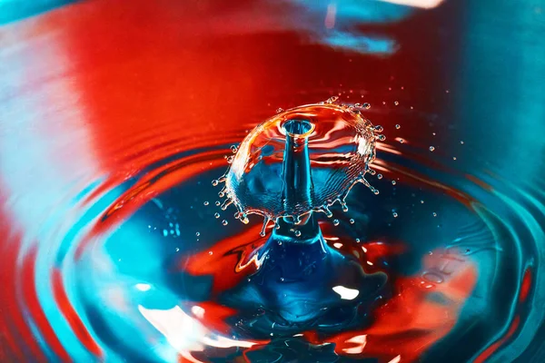 Μπλε και κόκκινο νερό με κυματισμούς και πιτσιλιές από δύο σταγόνες νερού που χτυπούν στον αέρα — Φωτογραφία Αρχείου