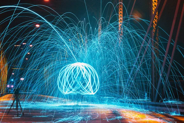 夜に橋の上の男の周りの複数の円で回転する明るい青色の火花 — ストック写真