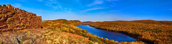 Panorama van reusachtig meer omringd door een eindeloze heuvels van een bos in de herfst en een bakstenen muur aan de linkerkant — Stockfoto