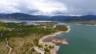 Dağılmış adalar ve dağlarla gölün üzerinde fırtına bulutları var.