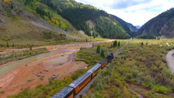 Aerial of locomotive train in mountain valley by stream leaving Silverton in Colorado — Stok Video