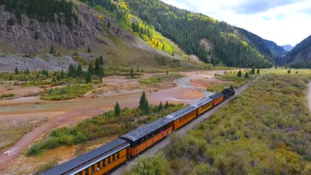 Terbang udara sepanjang kereta api lokomotif di lembah pegunungan dengan aliran meninggalkan Silverton untuk Durango di Colorado — Stok Video