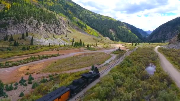 Aerial of locomotive train going through mountain valley by stream leaving Silverton to Durango in Colorado — Stok Video