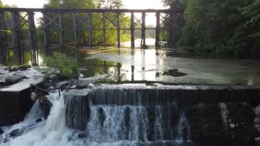 Arka planda şelaleler ve eski demiryolu köprüsü olan barajın üzerindeki havadan tava.