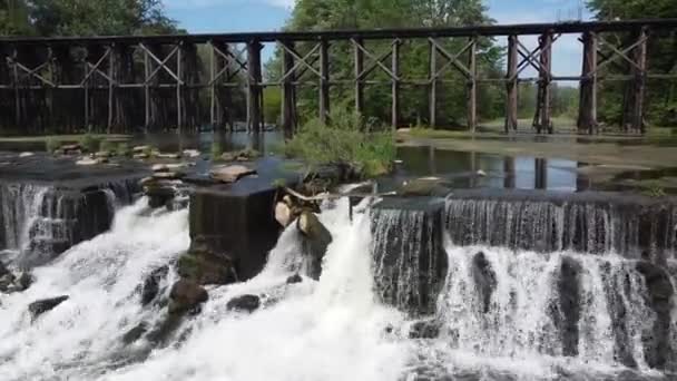Vol aérien vers le bas à côté du barrage avec cascades et vieux pont ferroviaire en arrière-plan — Video