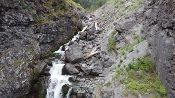 Aérienne à travers gorge à basse altitude avec vue sur des dizaines de petites chutes d'eau et des montagnes au loin par route de gravier — Video