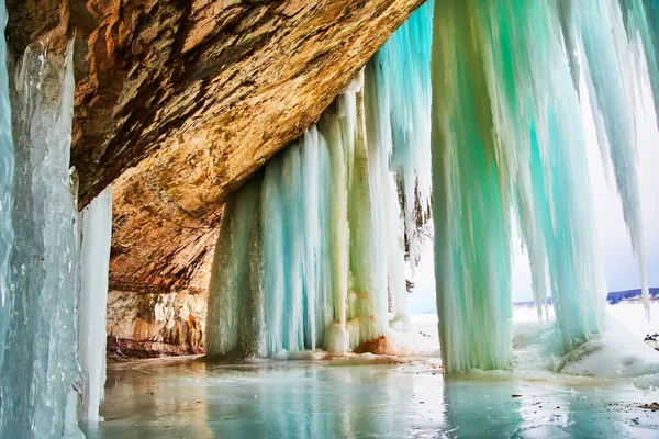 冬天的洞穴入口覆盖着蓝色和绿色的大冰柱 — 图库照片