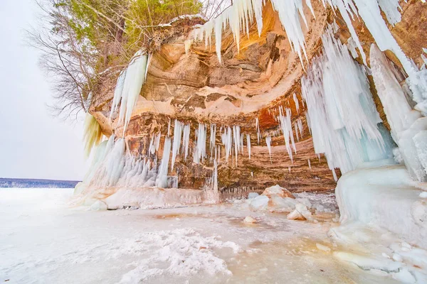 Ondulada cueva del acantilado en el lago congelado cubierto de carámbanos puntiagudos — Foto de Stock