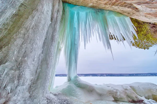 Grandes carámbanos azules colgando de rocas junto al lago congelado en invierno — Foto de Stock